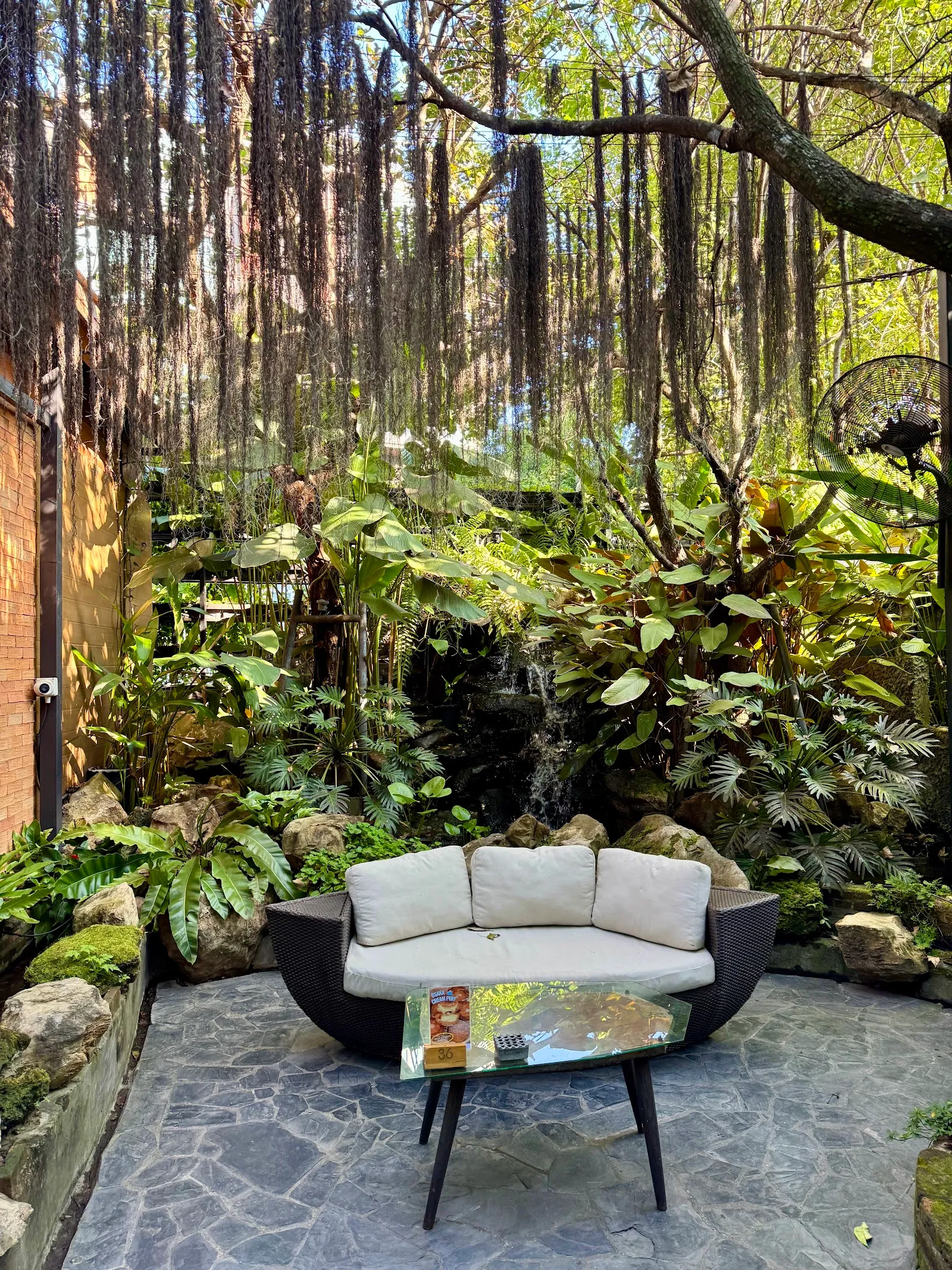 A round sofa under the trees beside a small waterfall in the garden
