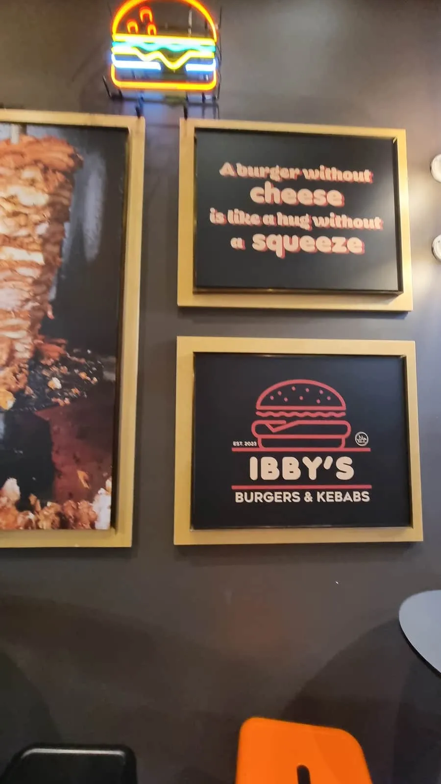 The Ibby’s interior wall — a burger neon, framed brand art and the doner spit