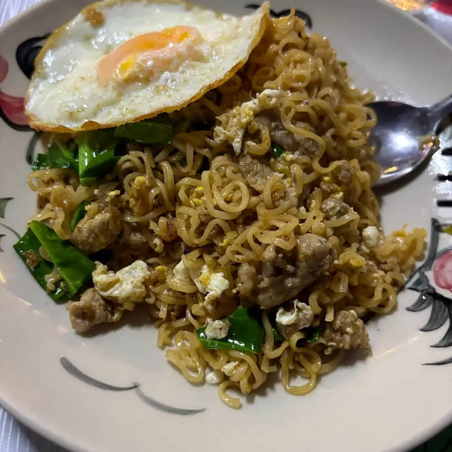 Stir-fried noodles with pork and a fried egg on a rooster plate
