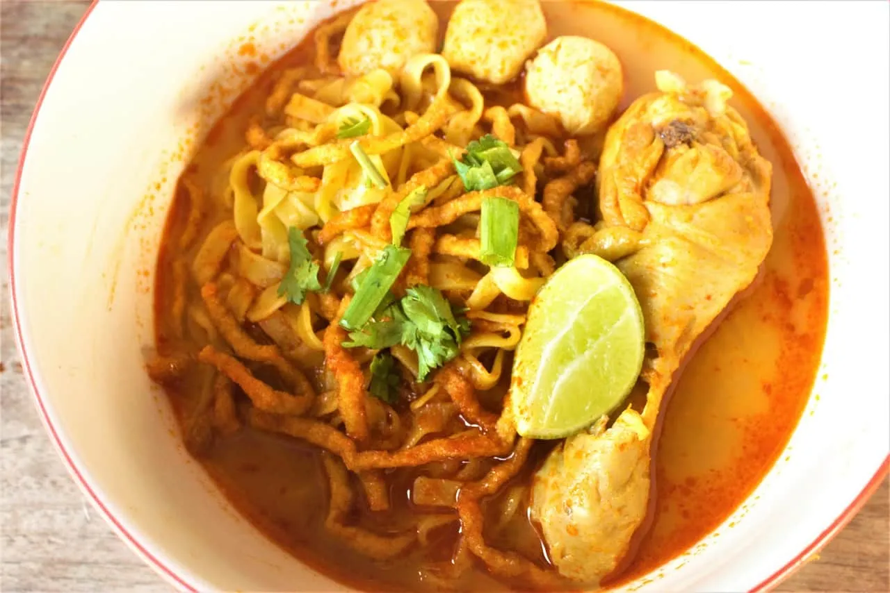A bowl of chicken khao soi — egg noodles in golden coconut curry, crispy noodles, lime and coriander