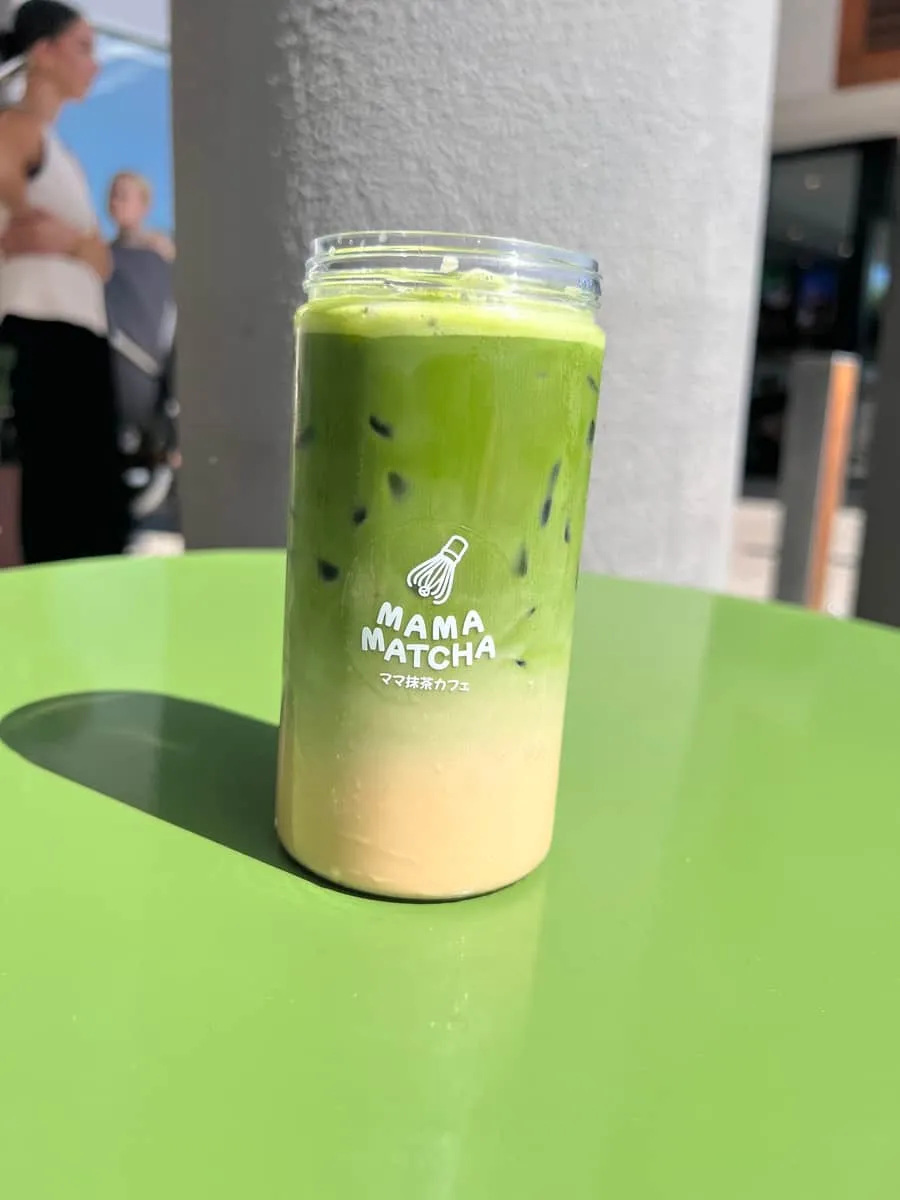 An iced matcha latte in a branded jar on a green table