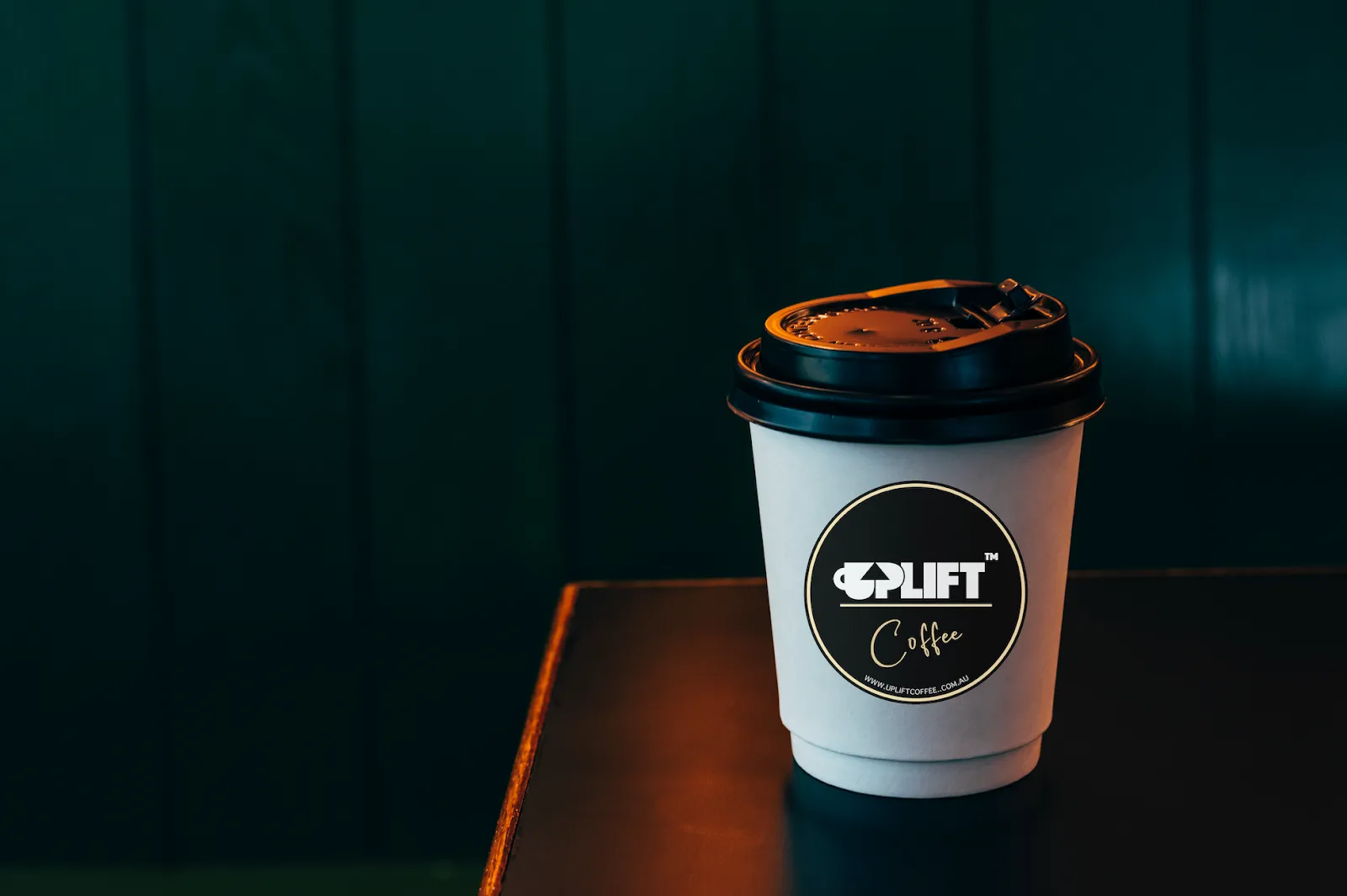Uplift Coffee takeaway cup on a deep-green wall